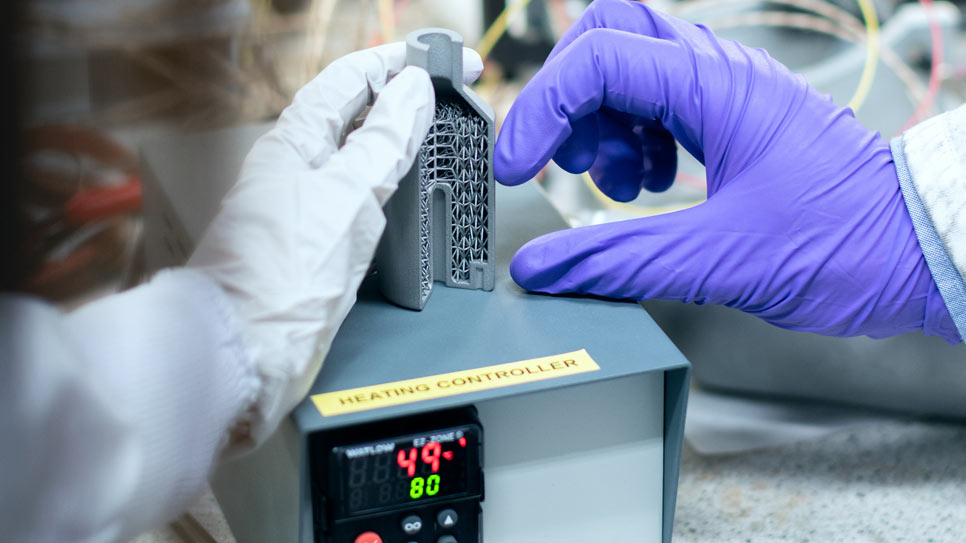 Operario con guantes manipulando una pieza impresa en 3D junto a un controlador de temperatura industrial
